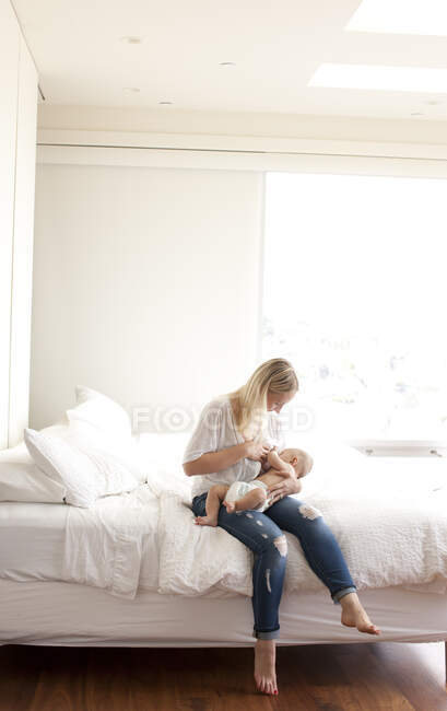Femme adulte moyenne assise sur le lit allaitant bébé fils — Photo de stock