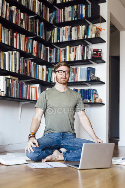 Hombre adulto sentado delante del portátil en posición de yoga - foto de stock