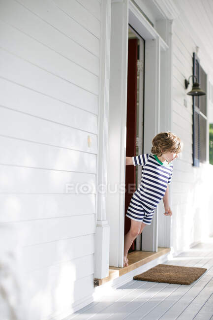 Boy leaning forward from front door onto porch — Stock Photo