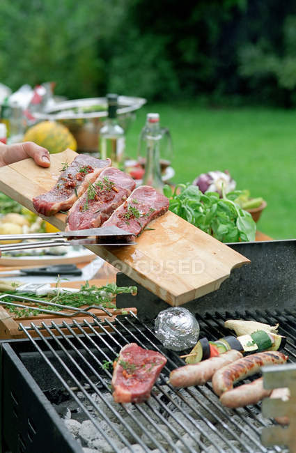 Image recadrée de l'homme mettant des steaks sur barbecue grill dans le jardin — Photo de stock