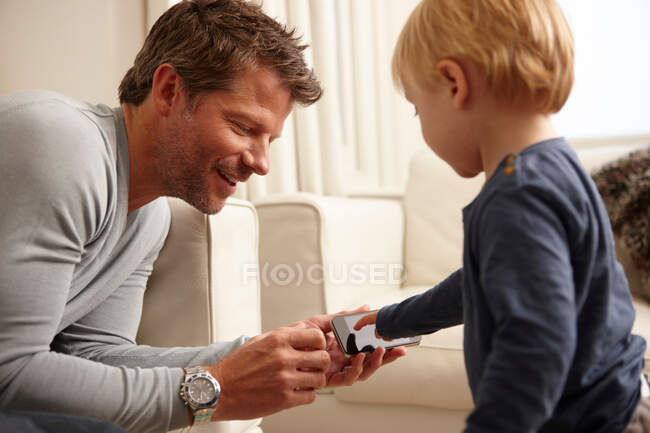 Padre sosteniendo el teléfono inteligente, hijo usando pantalla táctil - foto de stock