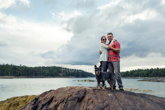 Retrato de casal adulto médio romântico e cachorro na rocha na costa do Maine, EUA — Fotografia de Stock
