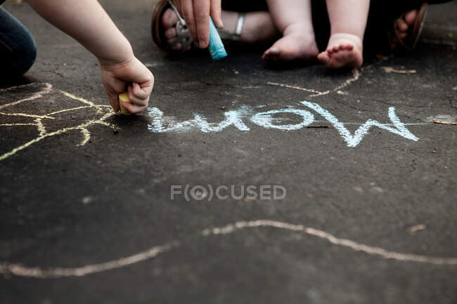 Madre y dos niños escribiendo en el suelo con tiza - foto de stock