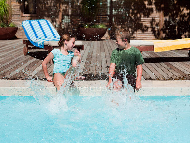 Chico y chica salpicando en la piscina - foto de stock