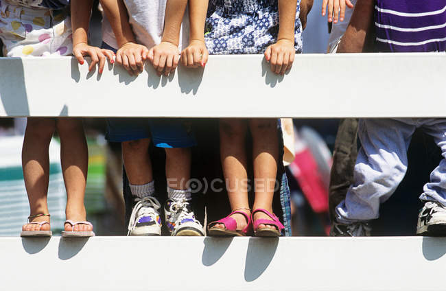 Tiro cortado de crianças encostadas à cerca à luz do sol — Fotografia de Stock