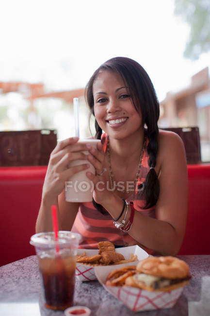Young woman holding milkshake in diner, smiling — Stock Photo