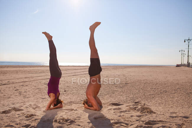 Mujer y hombre realizando handstands en la playa - foto de stock