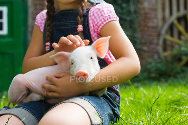 Кадр, на котором девочка держит поросенка, сидя на траве — стоковое фото