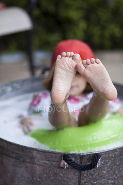 Chica sentada en baño de burbujas en el jardín con los pies sobresaliendo - foto de stock