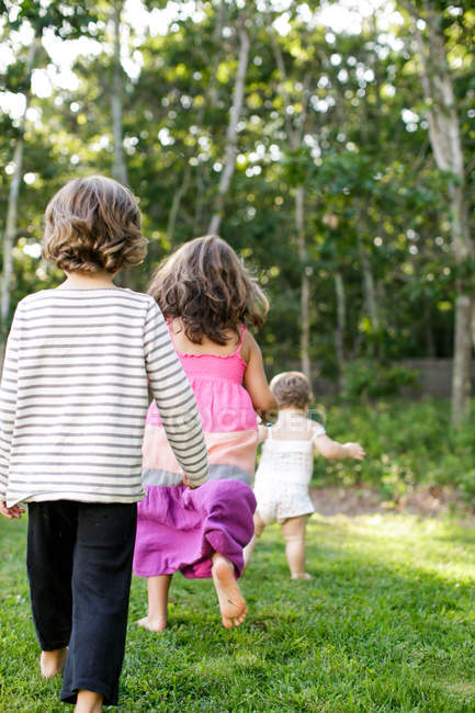 Rear view of female toddler followed by boy and girl in garden — Stock Photo