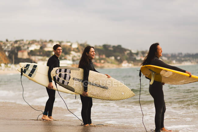 Three friends standing in sea, holding surfboards, preparing to surf — Stock Photo