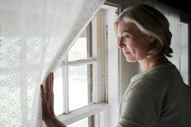 Mulher madura olhando pela janela — Fotografia de Stock