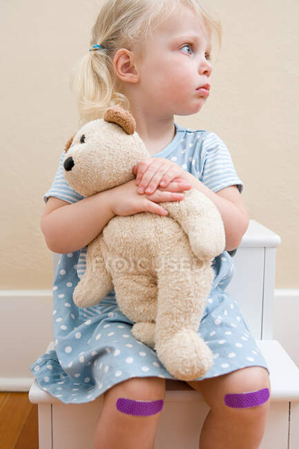 Chica con oso de peluche y yesos en las rodillas - foto de stock