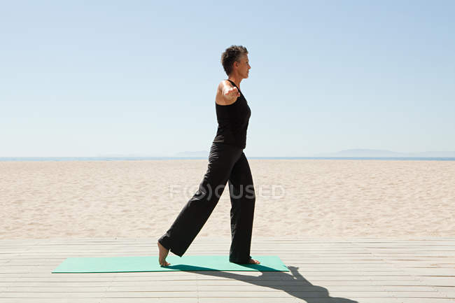Femme âgée faisant du yoga sur la plage — Photo de stock