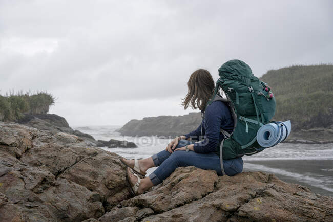 Jovem mulher com mochila, sentada na rocha, Constant Bay, Charleston, South Island, Nova Zelândia — Fotografia de Stock