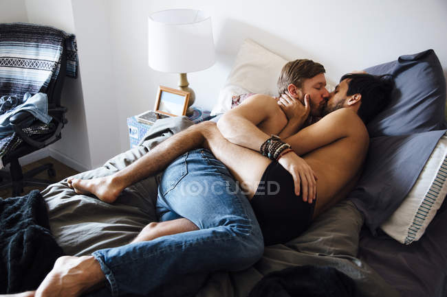 Чоловіча пара, частково одягнена, лежить на ліжку, цілується — стокове фото