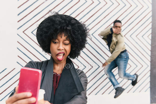 Mujer tomando selfie con amigo en frente de zig zag patrón de pared - foto de stock