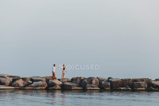 Distant view of couple holding hands on boulder wall, Lake Ontario, Toronto, Canada — Stock Photo
