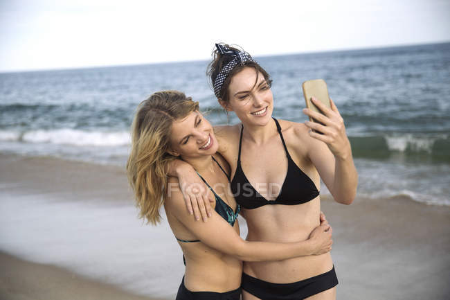 Женщины обнимаются и делают селфи с мобильным телефоном на пляже, Амагансетт, Нью-Йорк, США — стоковое фото