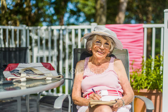Mulher sênior relaxante com livro em cadeira de praia — Fotografia de Stock