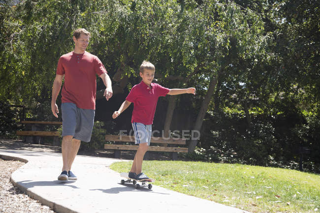 Мальчик с отцом практикуется на скейтборде в парке — стоковое фото