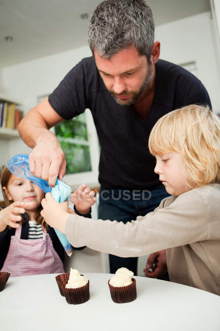 Hombre adulto medio y familia decorando cupcakes con glaseado - foto de stock