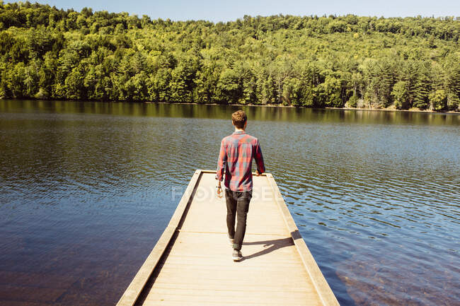 Человек идет по деревянному пирсу на озере, вид сзади — стоковое фото