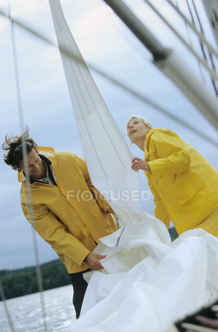 Couple taking down sail on boat — Stock Photo
