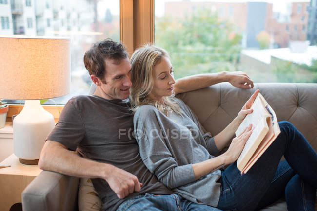 Paar legt sich auf Sofa und liest Buch — Stockfoto