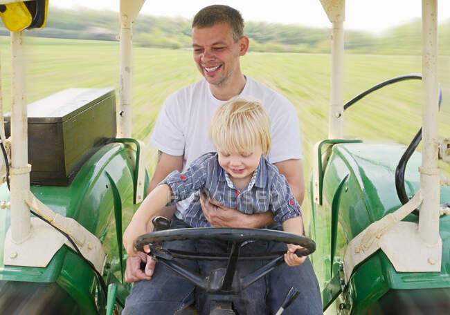 Mature man sitting with son in tractor, smiling — Stock Photo