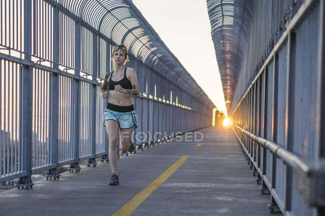 Young tattooed woman running on bridge with sunset behind — Stock Photo