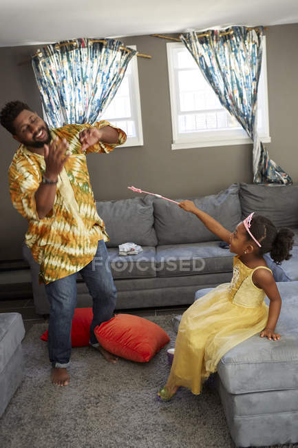 Menina em fantasia de fada lançando feitiço no pai na sala de estar — Fotografia de Stock