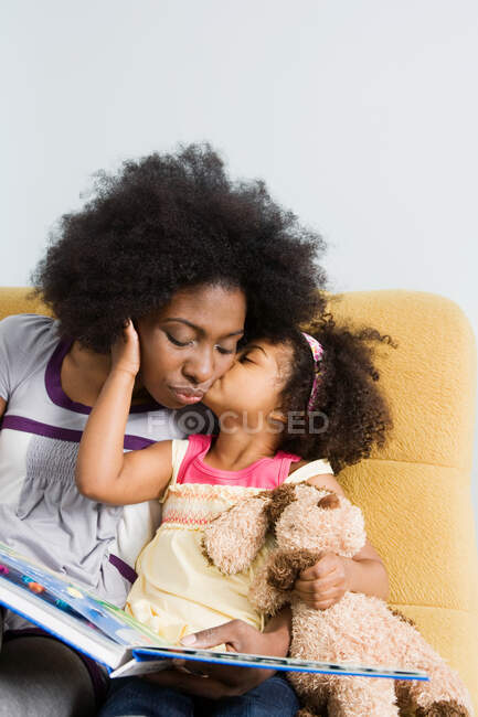 Una chica besando a su madre en la mejilla - foto de stock