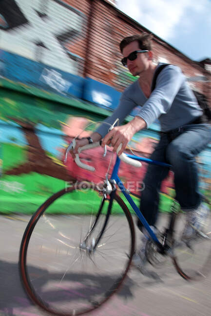 Mid adult cyclist riding passed graffiti — Stock Photo