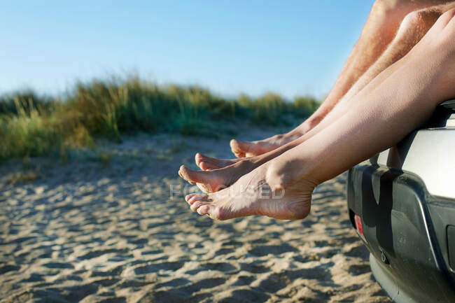 Couple adulte moyen assis pieds nus en voiture sur la plage — Photo de stock