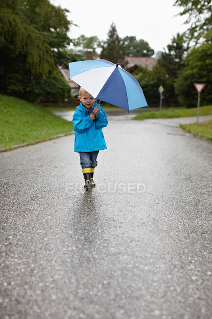 Toddler boy carrying umbrella on road — Stock Photo