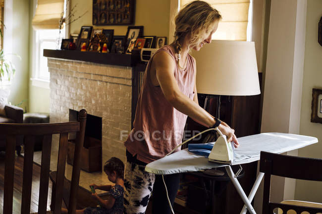 Жінка прасує в той час як дитина дочка грає на підлозі — стокове фото