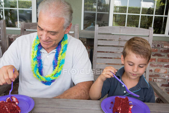 Nieto y hombre mayor comiendo pastel de cumpleaños - foto de stock