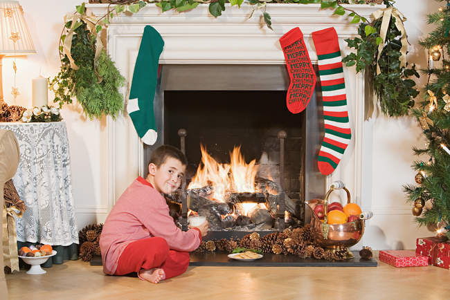 Boy sitting by fireplace at christmas — Stock Photo