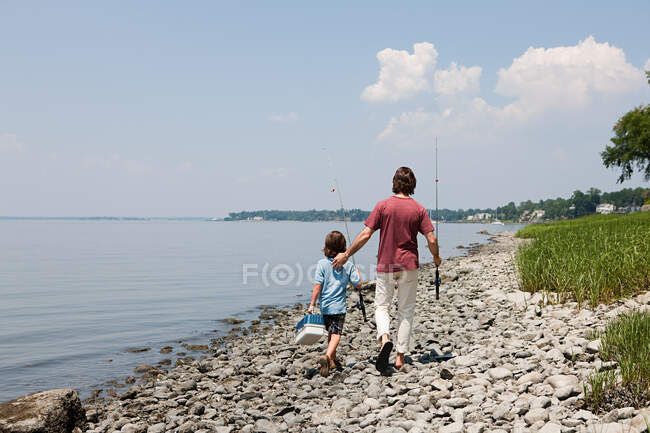 Padre e hijo caminando por la playa con cañas de pescar - foto de stock