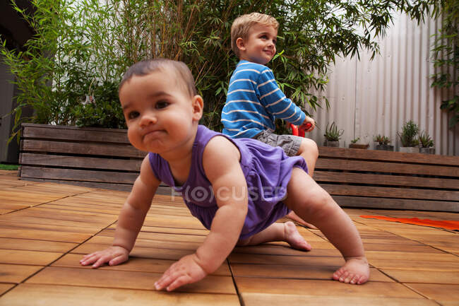 Bébé fille rampant sur le patio, frère en arrière-plan — Photo de stock