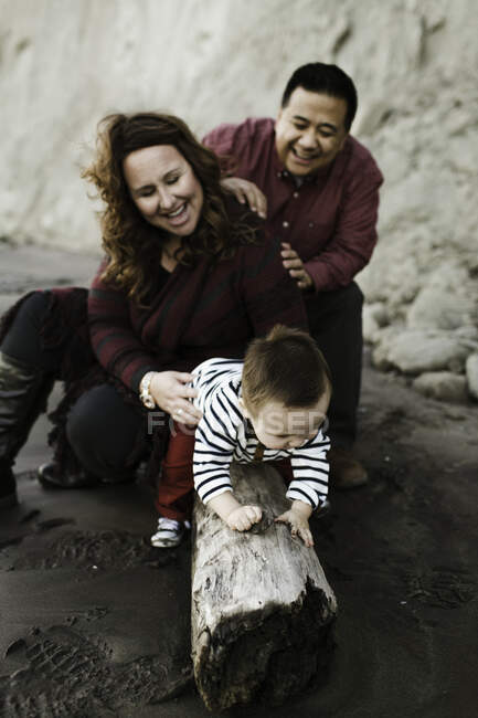 Família com bebê menino sentado em madeira à deriva na praia — Fotografia de Stock