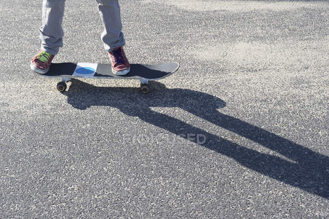 Detail of legs riding skateboard on asphalt with shadow — Stock Photo