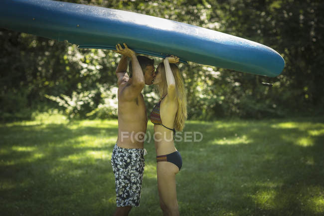 Romantic mature man kissing girlfriend whilst holding up kayak in garden — Stock Photo