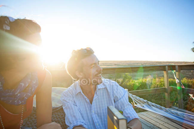 Jovem casal sentado na varanda ensolarada e sorrindo — Fotografia de Stock