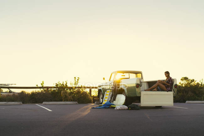 Young female surfer looking at smartphone in back of pickup truck at Newport Beach, California, USA — Stock Photo