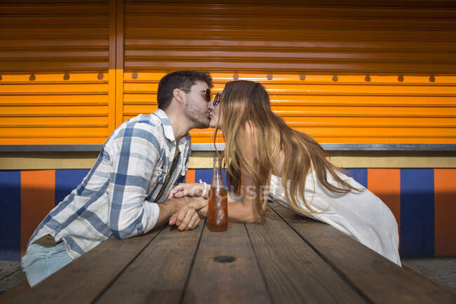 Pareja romántica pasar un buen rato besándose por mesa de picnic en el parque de atracciones - foto de stock