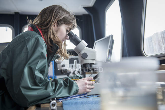 Ricercatrice che ispeziona il campione di plancton al microscopio su una nave da ricerca — Foto stock