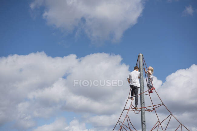 Hombre joven y niño escalando a la parte superior del marco de escalada - foto de stock