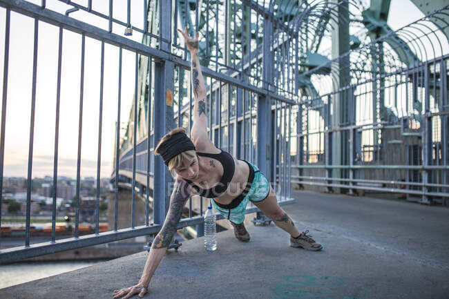 Joven mujer tatuada corriendo en el puente con puesta de sol detrás - foto de stock
